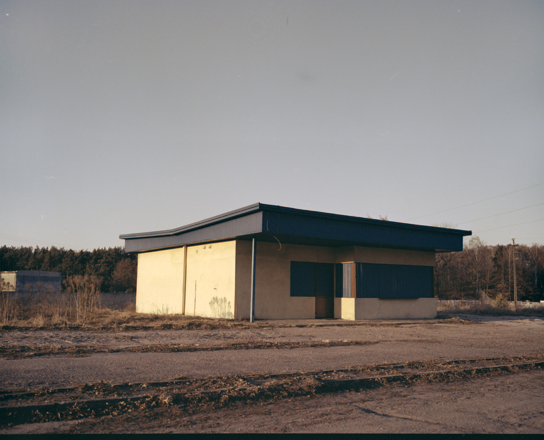 The same frame converted by Spool: a low grey sky over a shuttered roadside building, dry grass and broken asphalt
